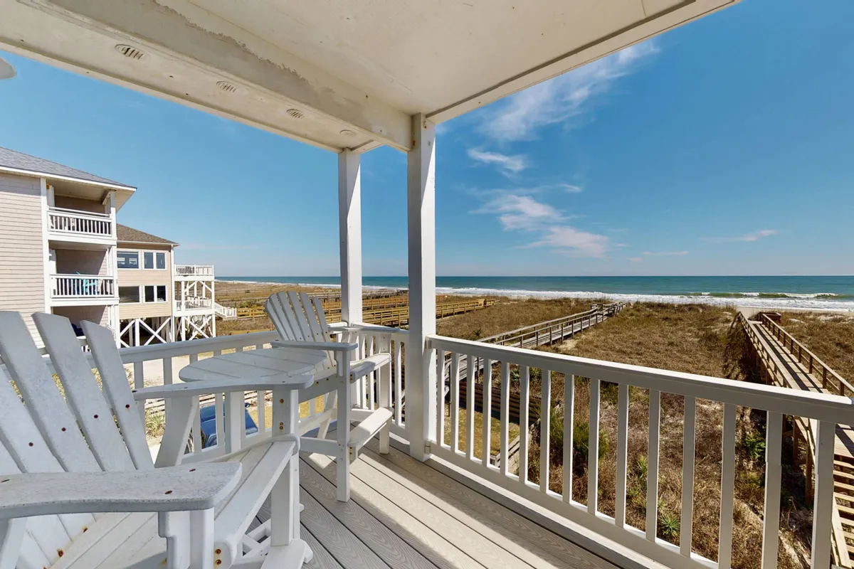 A tranquil exterior scene featuring deck chairs overlooking the beach, with a clear view of the ocean and a boardwalk stretching towards the water. The scene captures the relaxing atmosphere of unwinding on a private deck with the soothing sounds of the ocean in the background.