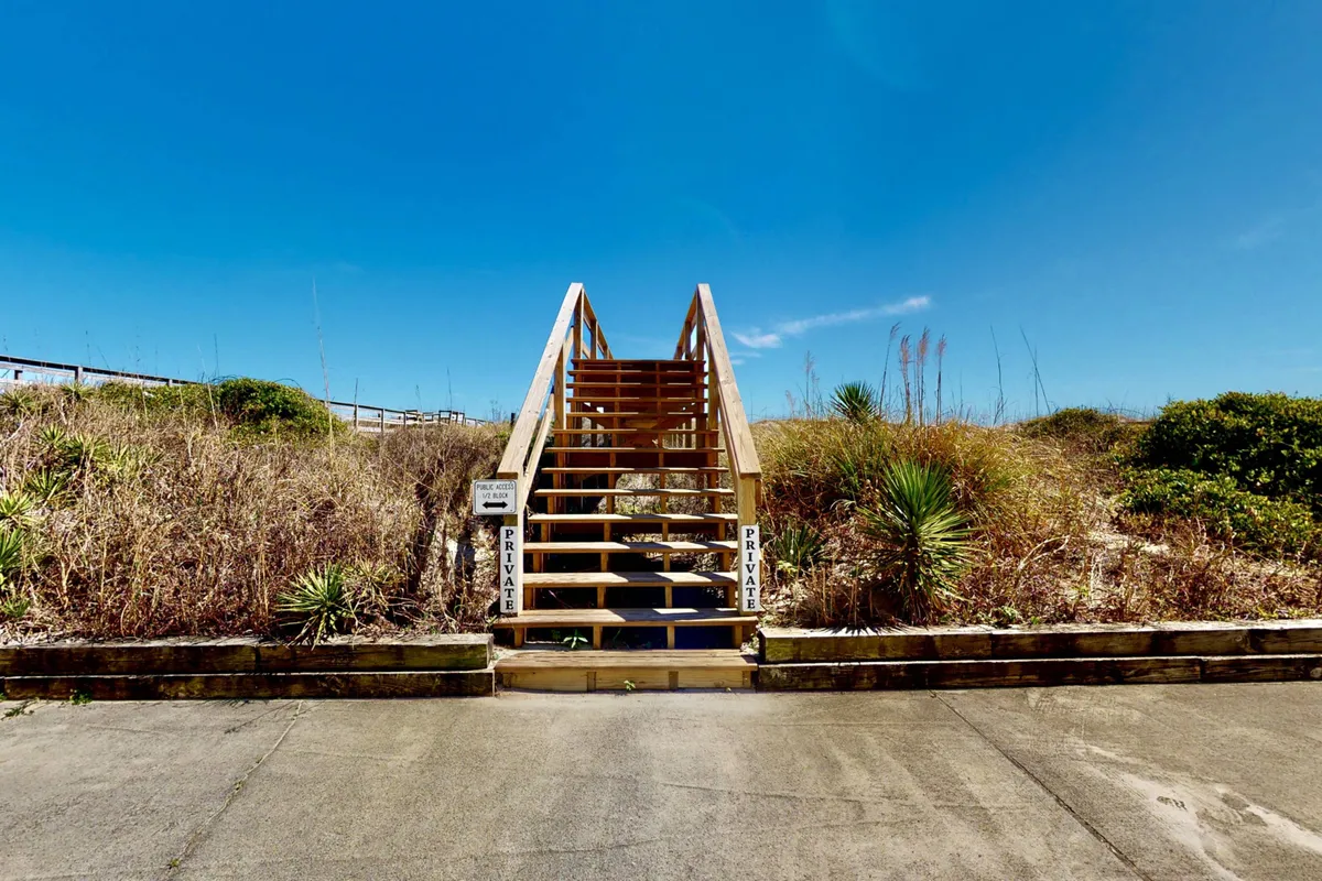A serene outdoor staircase surrounded by greenery leads directly to a private beach access point, with discrete signage indicating exclusivity. The natural setting emphasizes tranquility and privacy.